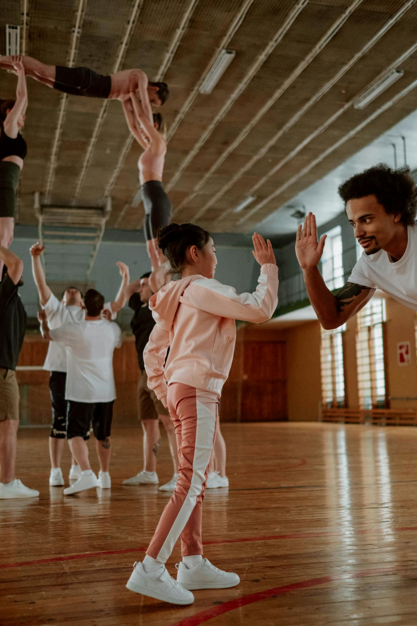 Cheerleaders practicing stunts and high five exchanges in a gym setting.